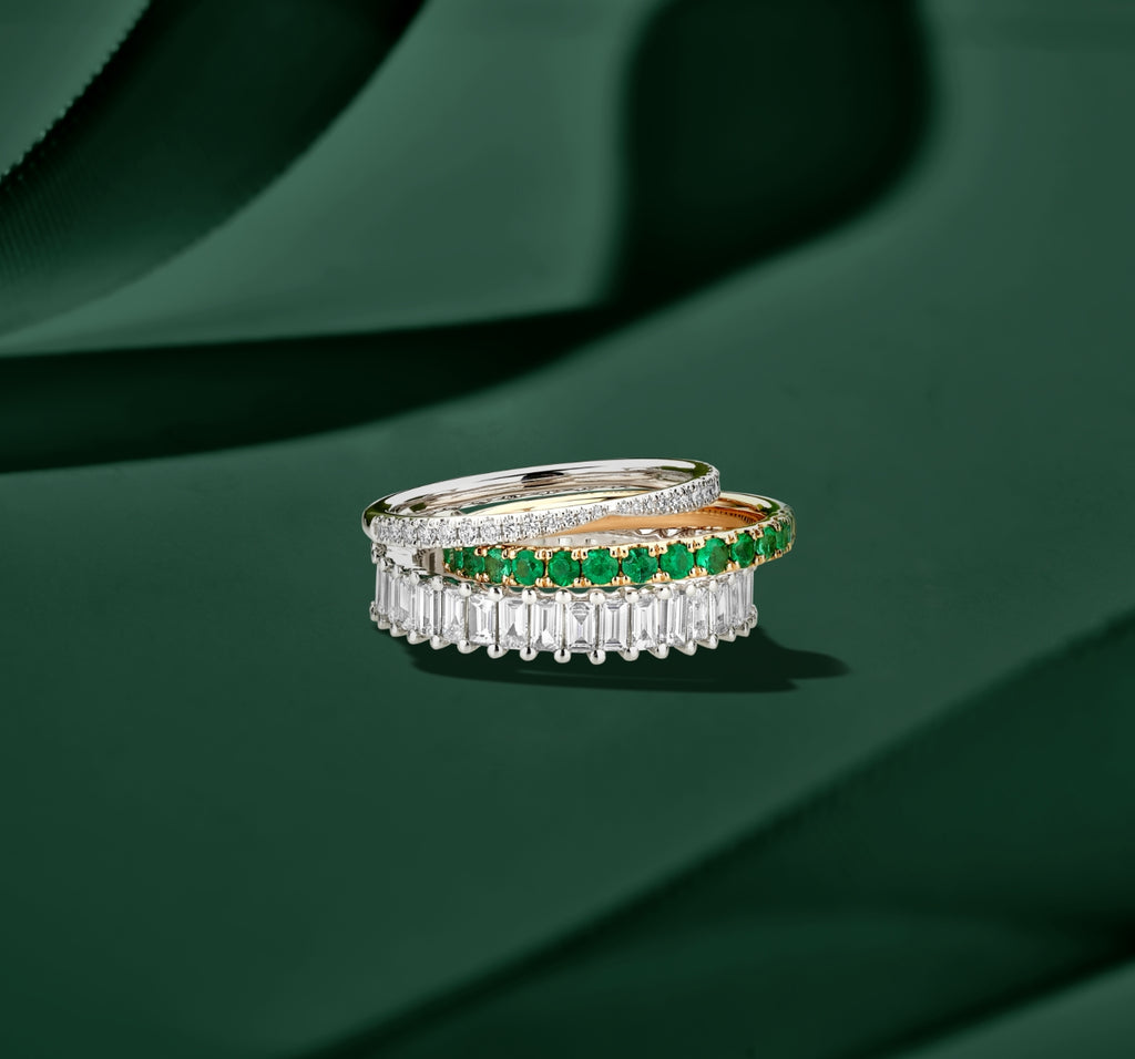ecksand white gold wedding rings with diamonds and rose gold ring with emeralds stacked on green background