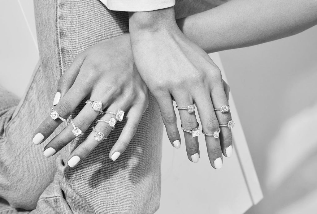 A collection of Canadian-made diamond engagement rings by Ecksand stacked on a model's hands in black and white.