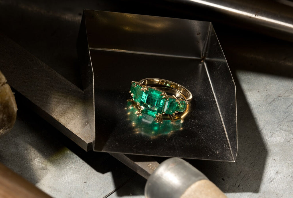 A Canadian-made five-stone emerald ring in 18K yellow gold, resting on a jeweler's workbench in our Montreal atelier.