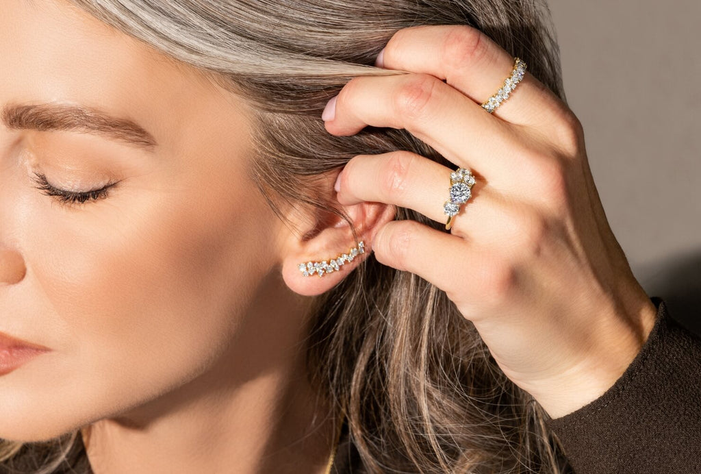 Model wearing Canadian-made diamond jewelry. An 18K yellow gold ear climber, engagement ring, and eternity wedding ring.