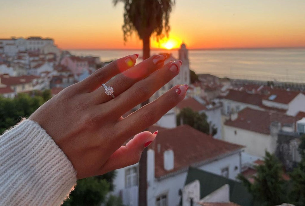 A woman's hand wearing an Ecksand Canadian-made diamond engagement ring in 18K white gold with a sunset view.