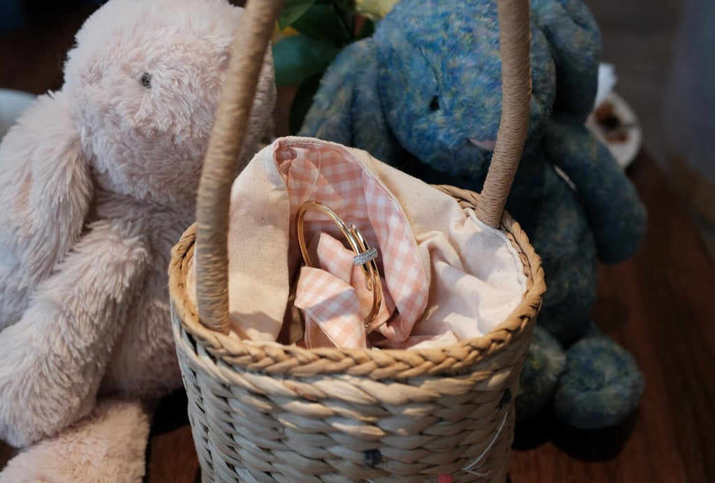 A Canadian-made 18K yellow gold diamond bangle sits in a wicker basket next to two stuffed bunnies.