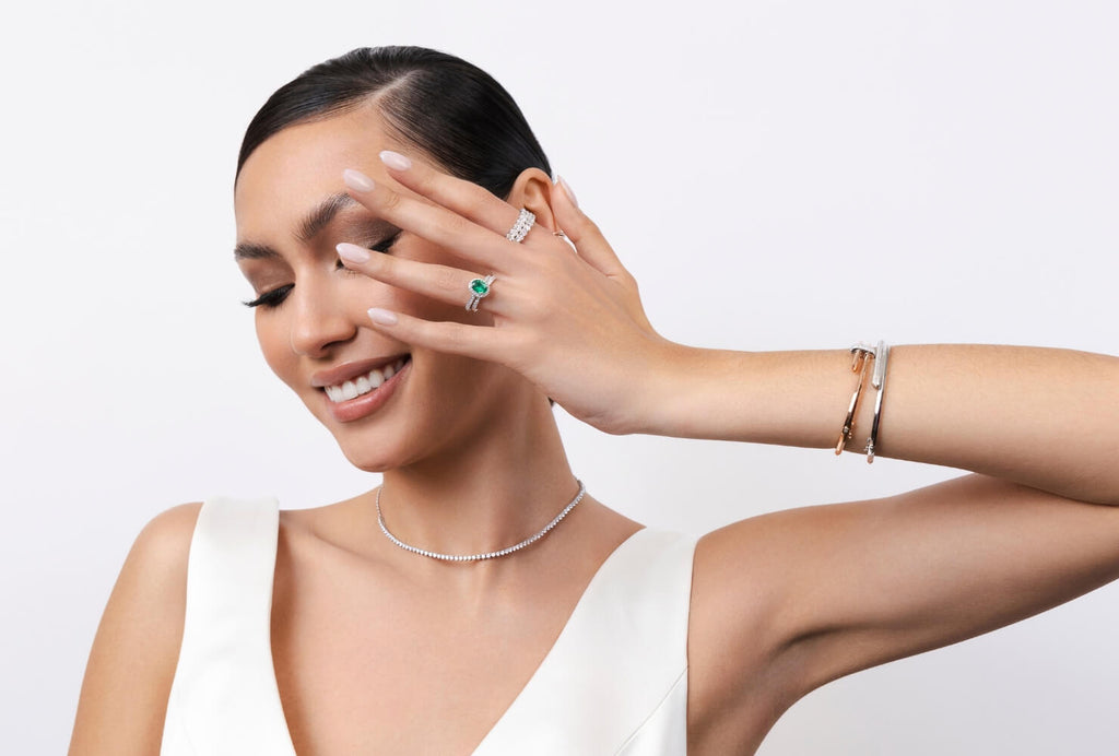 Model wearing a Canadian-made emerald engagement ring, diamond necklace, and white gold and rose gold bangles.