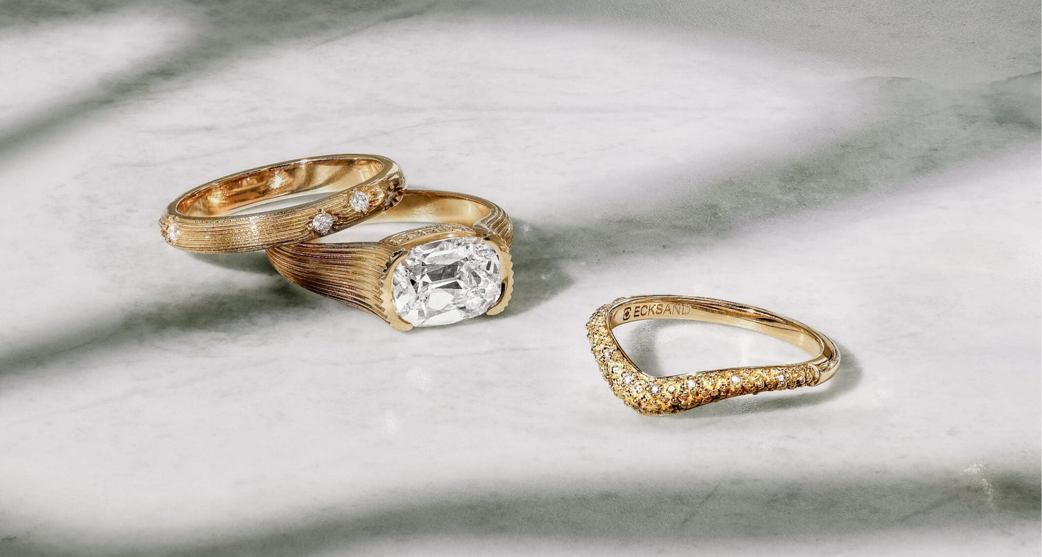 three canadian-made 18k yellow gold diamond rings from ecksand's dynasty collection, one an east west bezel hidden halo old mine diamond engagement ring, the others vintage textured band diamond pavé stackable wedding ring