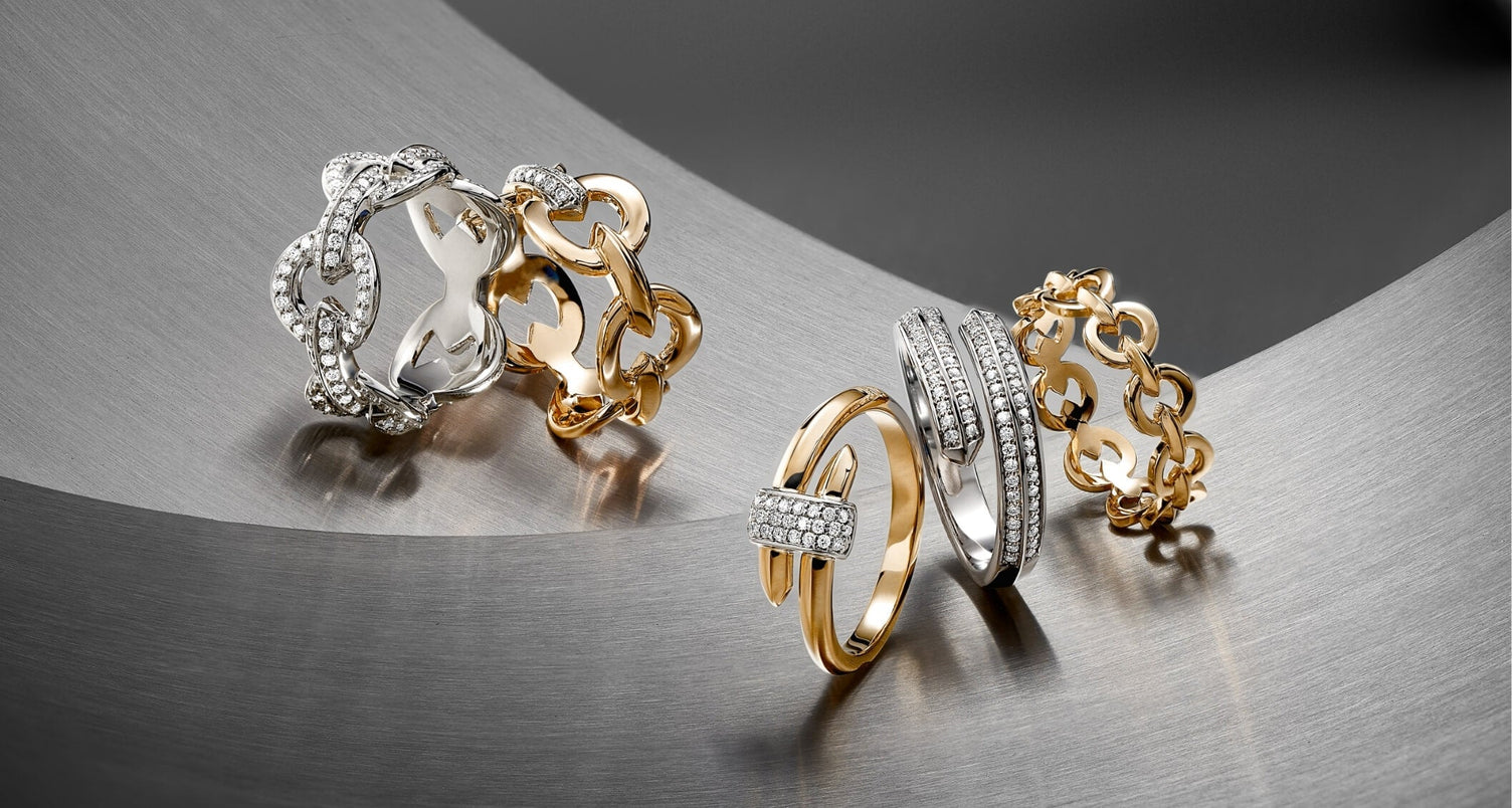 Canadian-made Ecksand diamond wrap rings in 18K white and yellow gold and diamond chain rings in 18k yellow gold on a brushed metal surface.