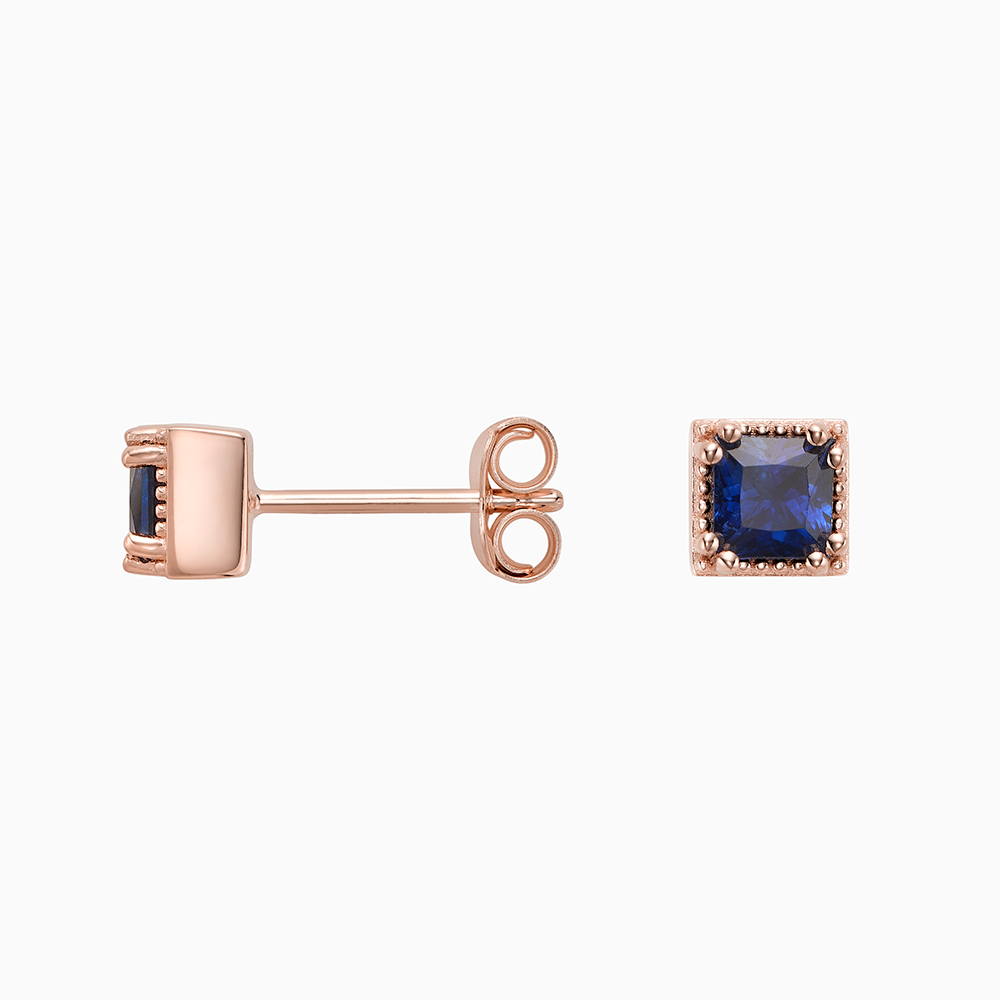 Angled view of Ecksand's Princess Blue Sapphire Stud Earrings with Milgrain Halo in 18k Rose Gold