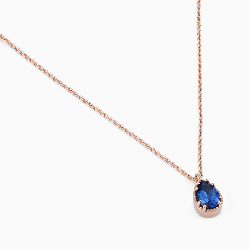 Angled view of Ecksand's Pear Blue Sapphire Stackable Necklace with Milgrain Halo in 18k Rose Gold