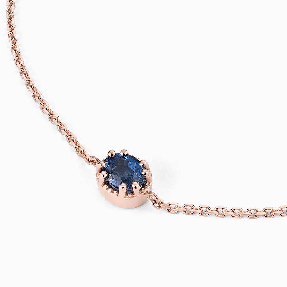 Angled view of Ecksand's Oval Blue Sapphire Stackable Bracelet with Milgrain Halo in 18k Rose Gold