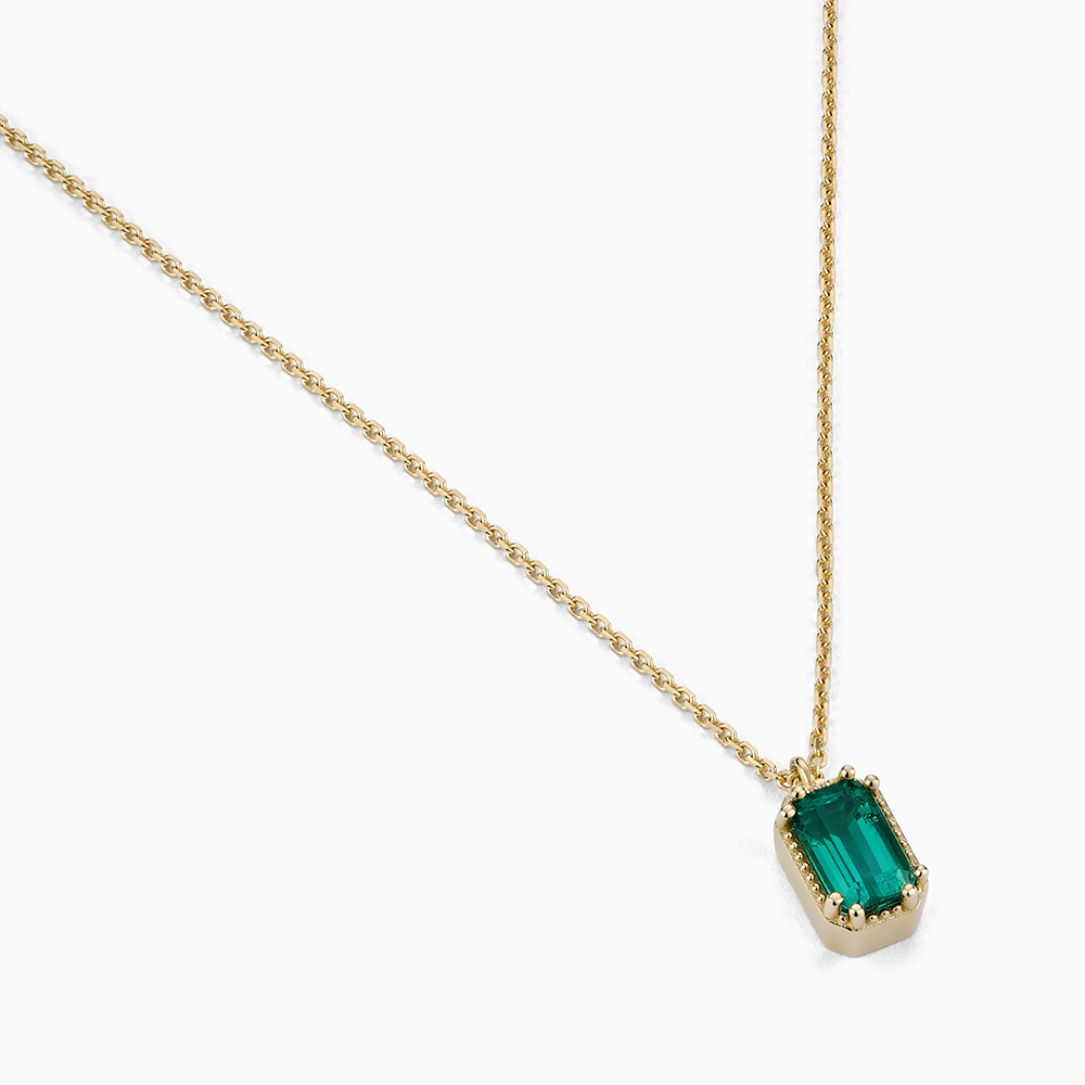 Angled view of Ecksand's Emerald Stackable Necklace with Milgrain Halo in 14k Yellow Gold