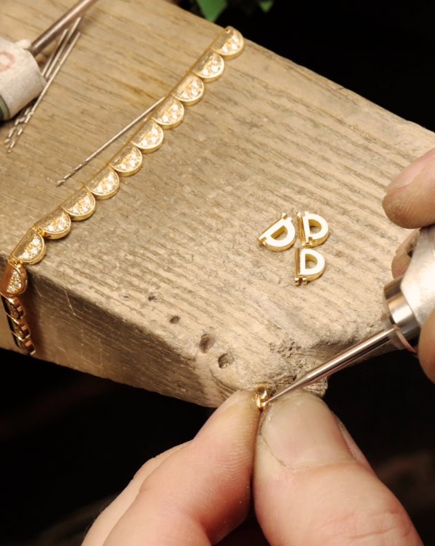 Jeweler’s hands working on small gold pieces at a wooden workbench, assembling delicate components of fine jewelry.