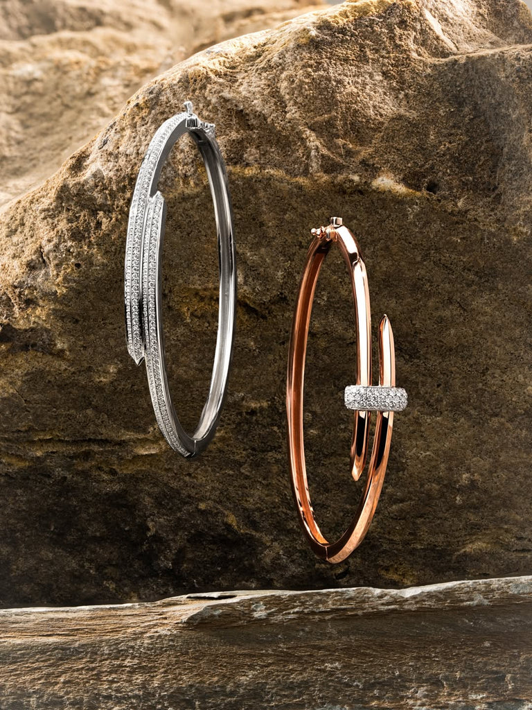 Two Ecksand diamond bangles in 18K roe gold and 18K white gold. Canadian-made fine jewelry on a rock surface.
