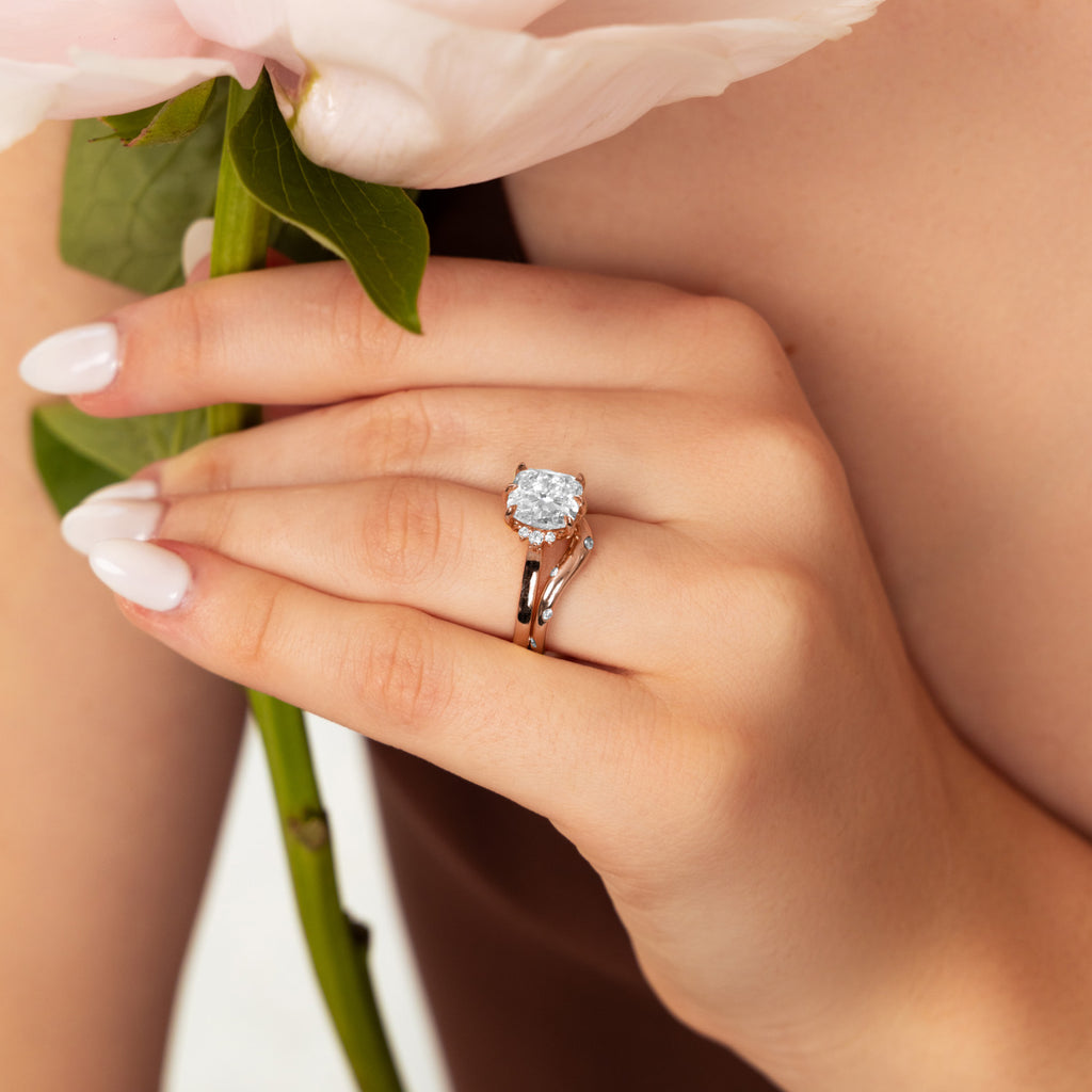 Model's hand with a Canadian-made 14K rose gold diamond bridal set, holding a pink flower.