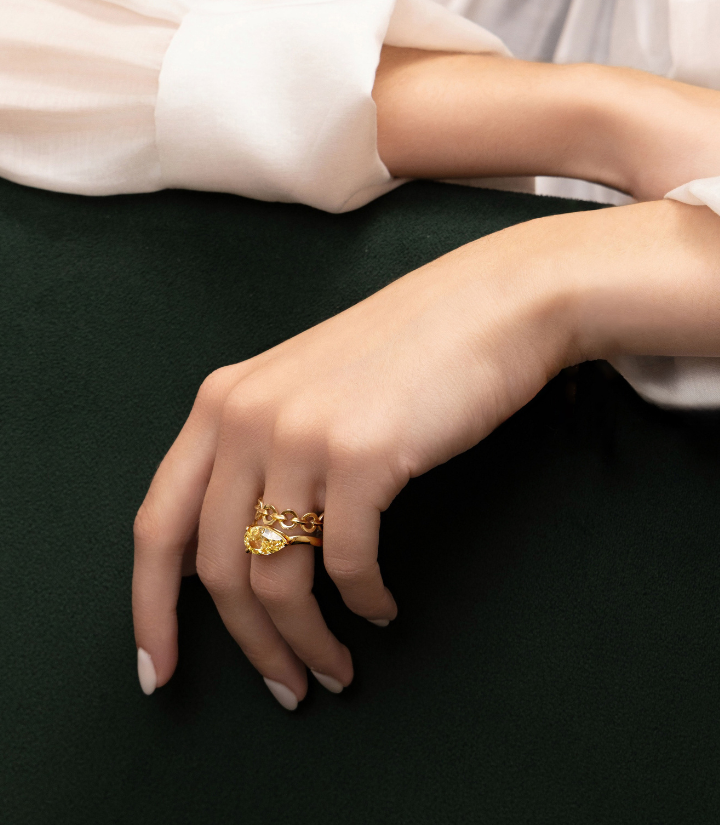 Model's hands showing Canadian-made diamond rings in yellow gold, including a pear yellow engagement ring and a chain ring.