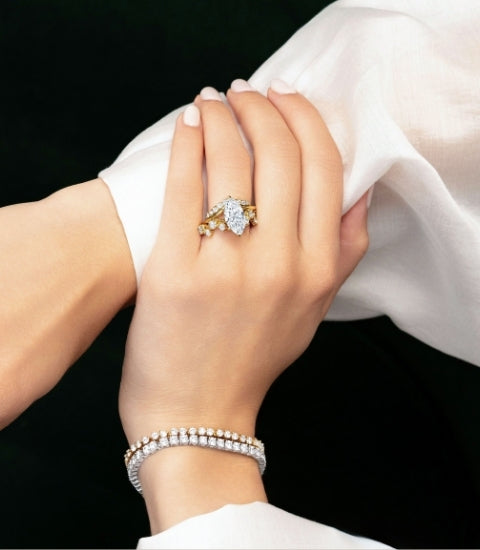 Model's hands showing Canadian-made diamond rings in yellow gold, including a marquise diamond engagement ring, a curved diamond wedding ring, and a tennis bracelet.