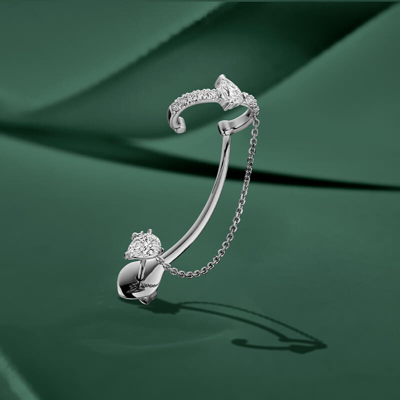 ecksand white gold statement cuff earring with diamonds and chain on green background