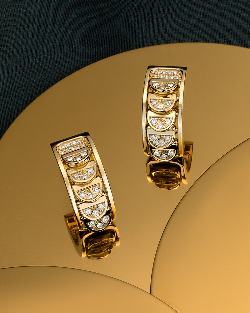 Canadian-made 18k yellow gold earrings with diamond accents on a gold surface and black background.