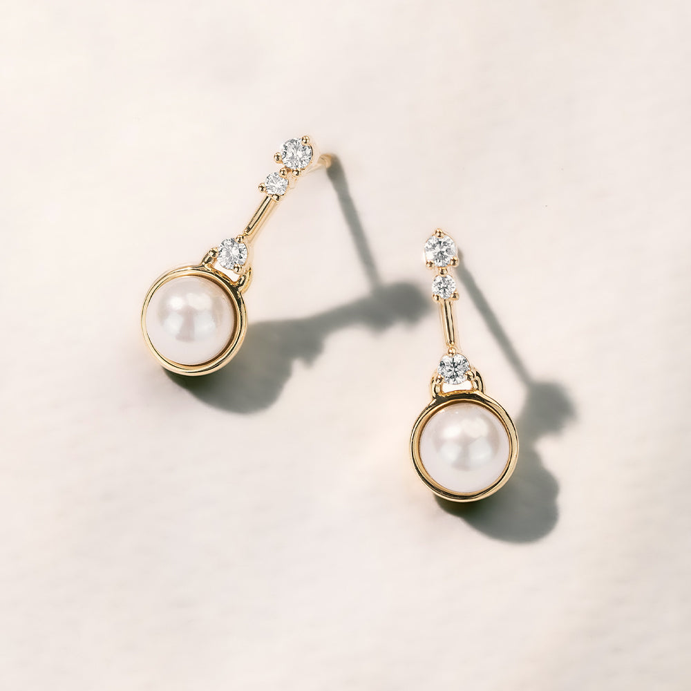 Pair of pearl earrings with gold and diamond accents on a light background