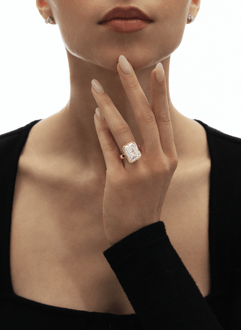 Close-up of a hand wearing a canadian-made 18k yellow gold emerald diamond ring on a white background