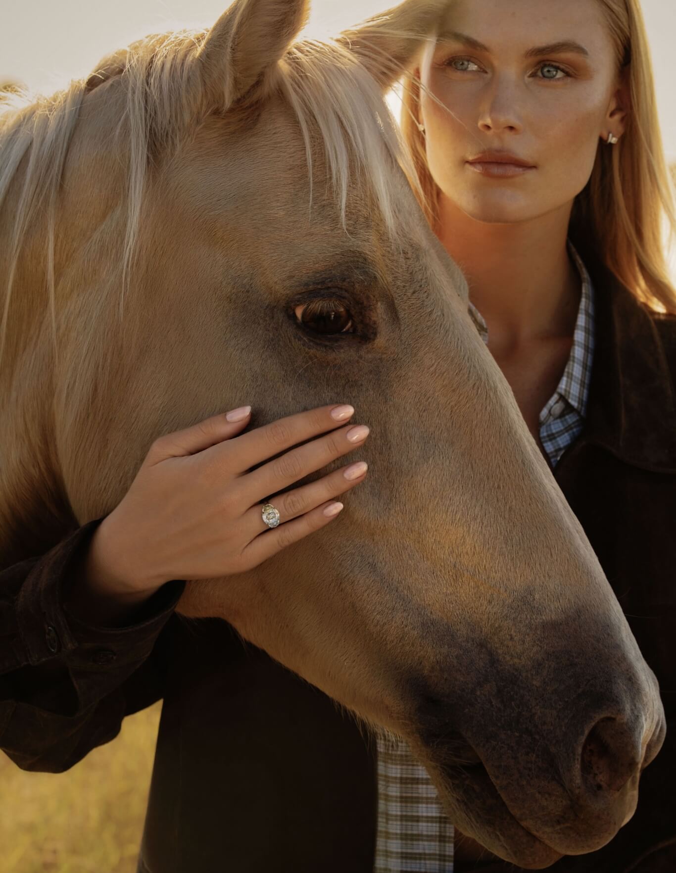 model wearing canadian-made 18k yellow gold ecksand dynasty three stone old mine diamond engagement ring in a field with a horse