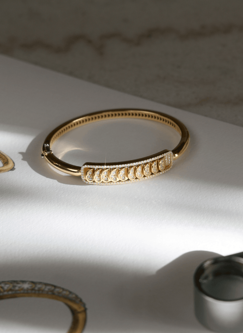 A canadian-made 18k yellow gold reversible bangle bracelet with a pavé-set row of clear stones across the front, displayed on a white surface with soft shadows.