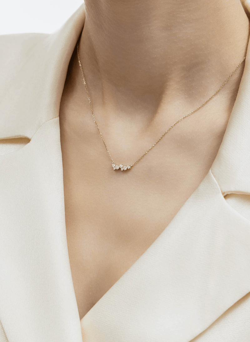 A delicate 18k yellow gold chain necklace with a small cluster of diamonds at the center, worn by a model in a cream-colored blazer.