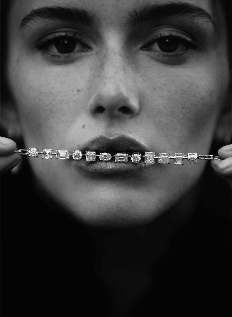 A close-up black and white portrait of a woman holding a canadian-made 18k white gold diamond bracelet across her mouth, with her eyes looking directly forward.
