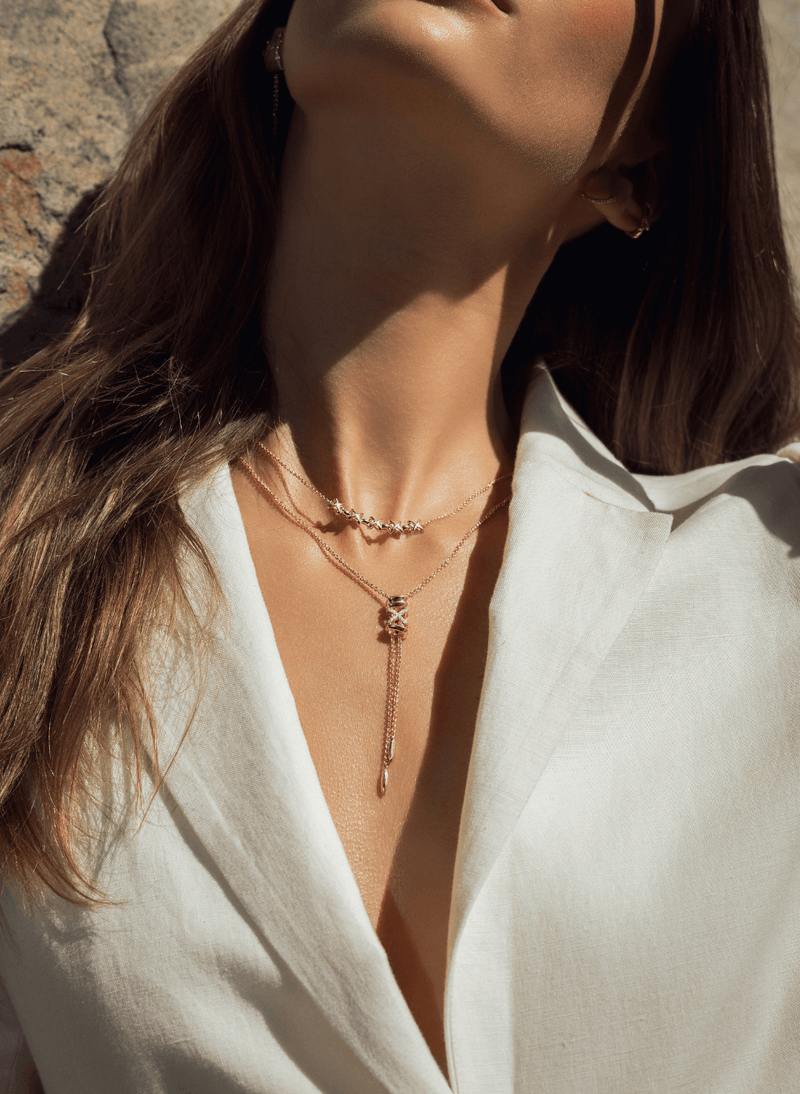 A close-up lifestyle shot of a woman wearing a layered canadian-made 14k rose gold necklace set, featuring a lariat necklace, styled with a white collared shirt.