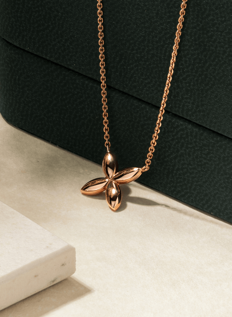 A canadian-made 18k rose gold necklace with a butterfly pendant, displayed on a textured dark green surface and a light beige marble block.