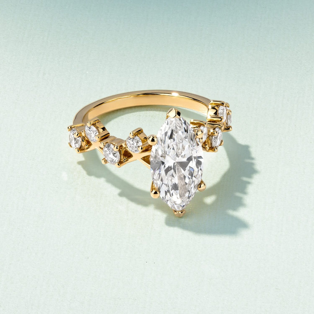a yellow gold ecksand diamond engagement ring with a marquise diamond on a green background