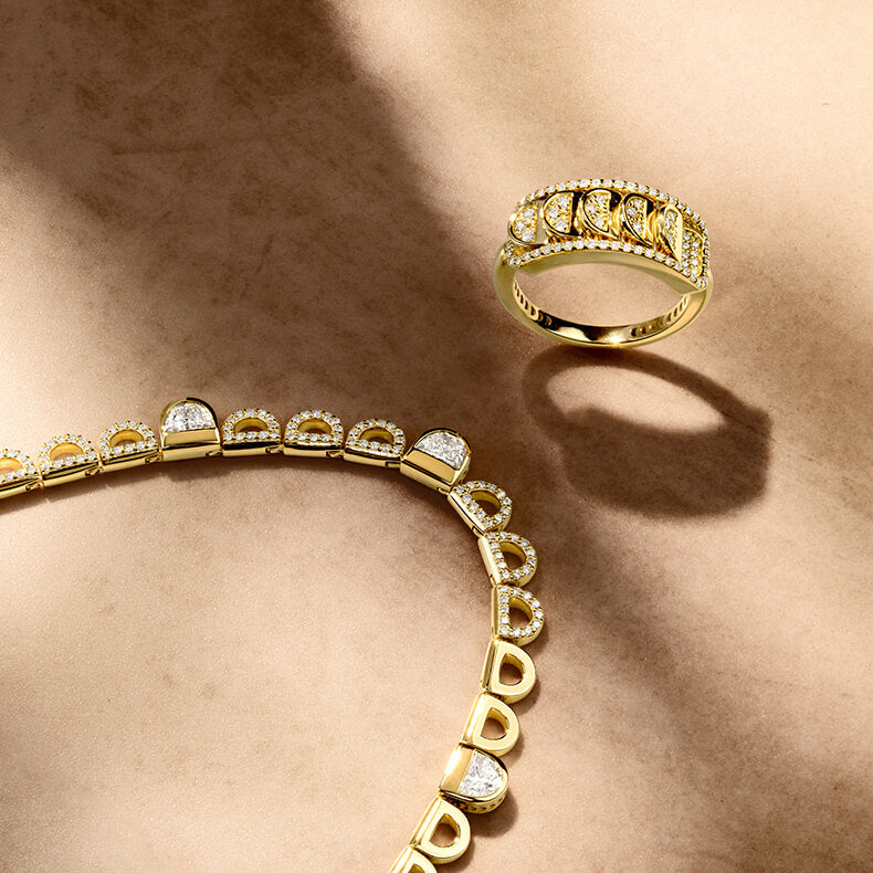 Canadian-made set of 18K yellow gold diamond chain necklace with diamond accents and an 18k yellow gold diamond pave ring on textured background.