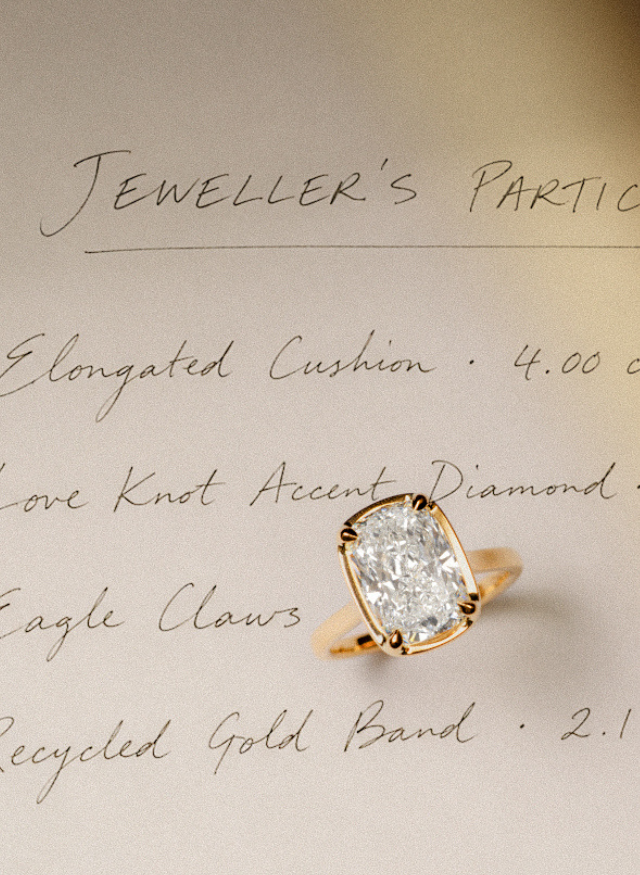 A canadian-made 18k yellow gold ring with an elongated cushion-cut diamond set on a beige paper background with handwritten notes detailing the ring's features.