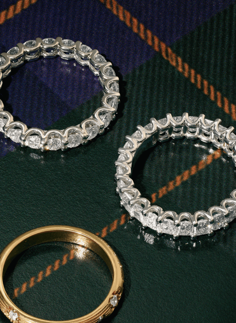 Two canadian-made 18k white gold diamond eternity rings with clear gemstones and a gold band, arranged on a dark green and navy tartan plaid fabric background.