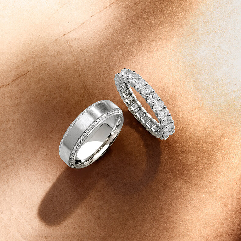 Two Canadian-made 18K white gold wedding rings with diamonds, including a classic brushed band with diamond pavé and a diamond eternity band, on a textured background