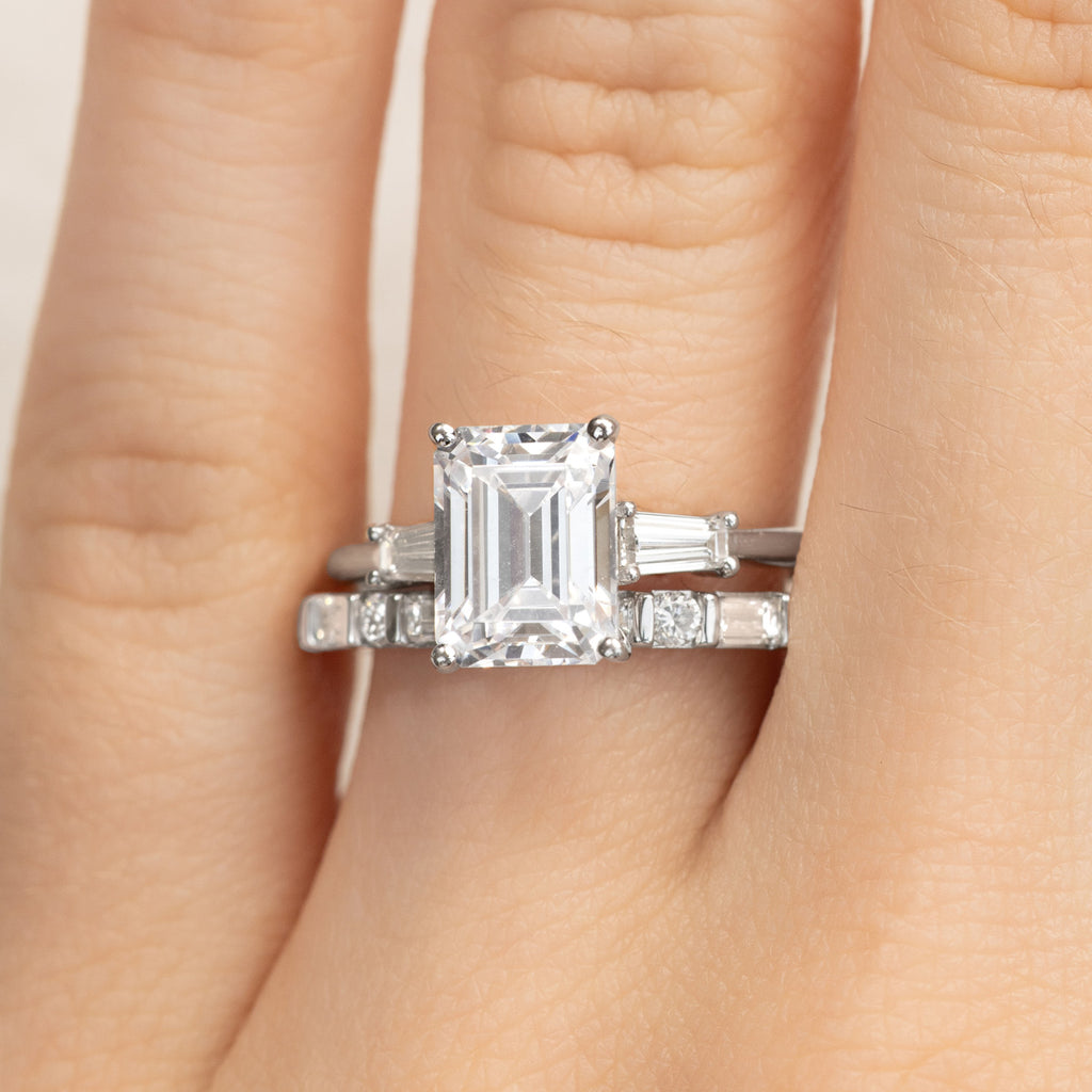 A Canadian-made emerald-cut diamond engagement ring and wedding ring bridal set in 18K white gold, worn on a model's hand.