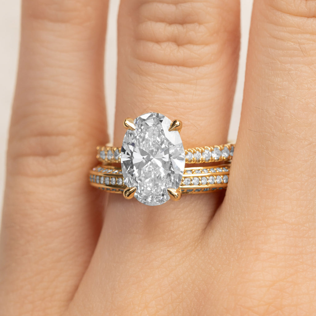 A hand wearing a Canadian-made bridal stack featuring an oval diamond engagement ring and two pavé bands in 18K yellow gold.