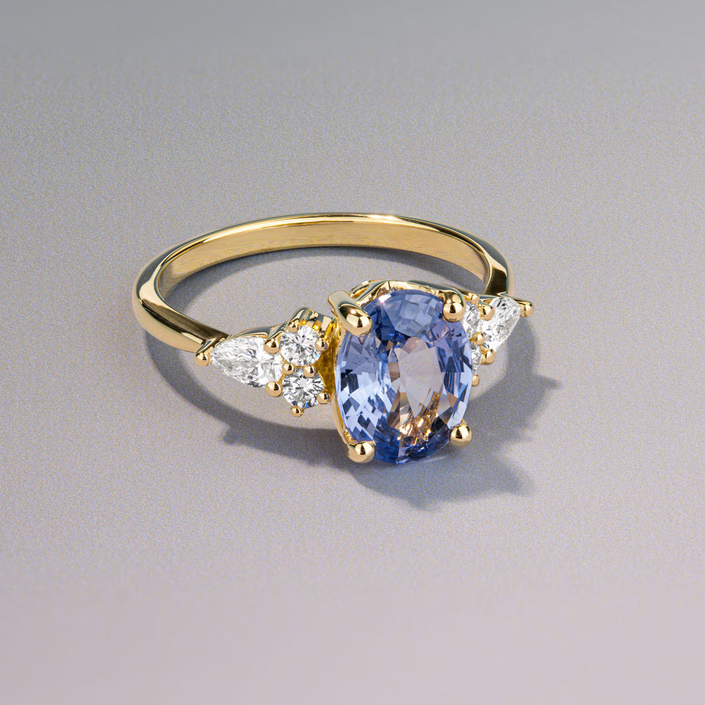 A Canadian-made oval sapphire engagement ring with pear and round diamonds on an 18K yellow gold band.