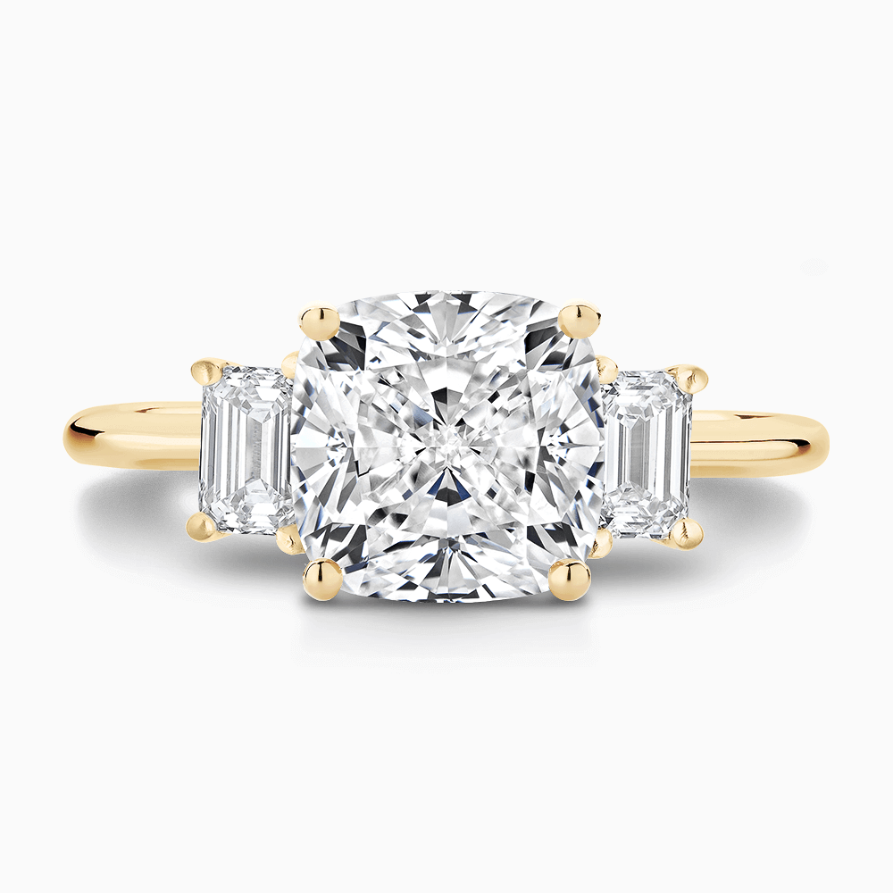 The Ecksand Three-Stone Diamond Engagement Ring with Basket Setting shown with Cushion in 18k Yellow Gold